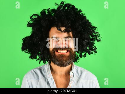 Uomo divertente con parrucca nera. Uomo con barba e baffi in periwig ricci. Hipster barbuto in parrucca afro riccia nera. Barbiere. Ragazzo elegante con capelli neri Foto Stock