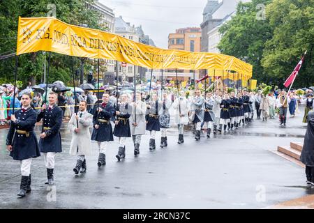 RIGA, LETTONIA, 2 LUGLIO 2023: I partecipanti alla parata di apertura del Festival della canzone e della danza lettone nazionale portano un lungo striscione giallo Foto Stock