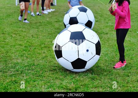 Bambini che giocano a una gigantesca palla da calcio su un campo verde. Attività divertenti per bambini e sfondo per eventi all'aperto. Foto Stock