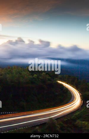 Il paesaggio della strada di montagna all'alba, i sentieri illuminati sulla curva della strada di montagna e il suggestivo cielo dell'alba sullo sfondo. Foto Stock