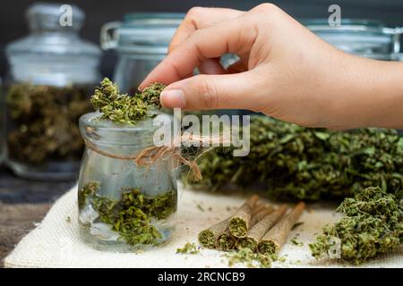 Una donna che tiene fiori di marijuana in una bottiglia di vetro trasparente Foto Stock