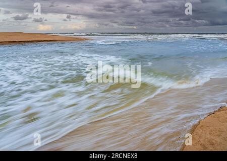 L'acqua che scorre verso il mare da un fiume costiero tra i bar di sabbia a Currimundi sulla Sunshine Coast nel Queensland, Australia Foto Stock