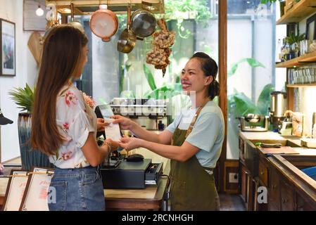 Giovane cameriera vietnamita che lavora con la macchina per il check-out e clienti al bar Foto Stock