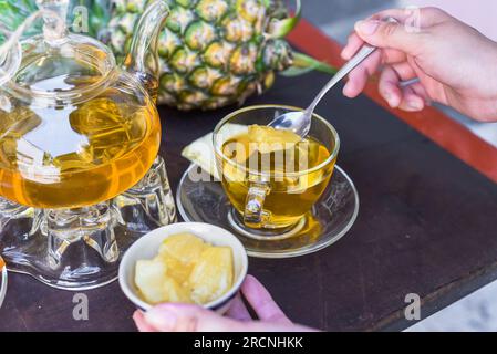Teiera di vetro con tè all'ananas e marmellata di casa, tazze e frutta cristallizzata su sfondo scuro Foto Stock