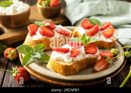 Sandwich con fragole e formaggio morbido su fondo di legno. Pane tostato alle bacche, cibo sano. Foto Stock