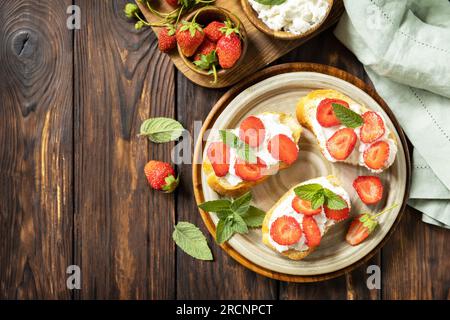 Sandwich con fragole e formaggio morbido su fondo di legno. Pane tostato alle bacche, cibo sano. Vista dall'alto. Foto Stock