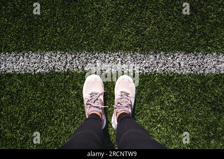 Gambe di una donna in piedi su un parco giochi sportivo dietro una linea di partenza bianca Foto Stock