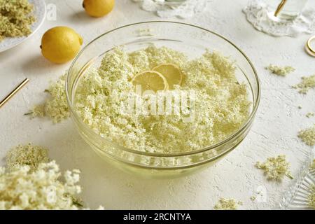 Fiori di sambuco raccolti in maceratina primaverile in una ciotola d'acqua con limone, per preparare lo sciroppo alle erbe Foto Stock