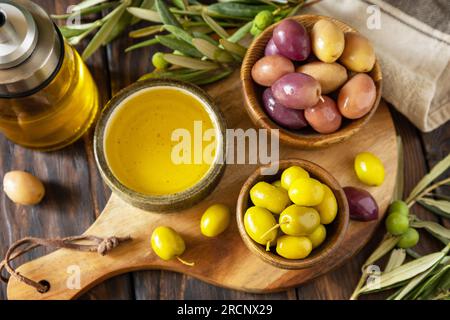 Olive appena raccolte frutti di bosco in ciotole di legno e olio pressato servito su vecchie tavole di legno. Foto Stock