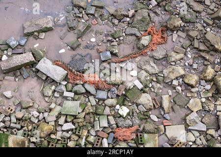 Vecchia corda, mattoni e rocce sparsi sulla riva del Tamigi, vista della riva del fiume dall'alto a North Woolwich, East London, Inghilterra, Regno Unito. Foto Stock