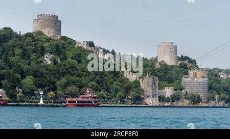Fortezza di Rumeli circondata da alberi su una collina sulle rive del Mare del Bosforo con un traghetto passeggeri rosso attraccato, Istanbul, Turchia Foto Stock