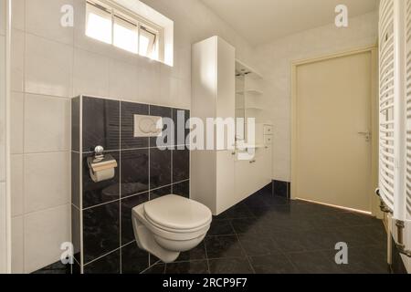 bagno con piastrelle bianche e nere alle pareti, rotoli di carta igienica davanti alla porta della camera Foto Stock