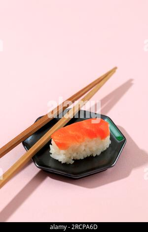 Un sushi al salmone Nigiri su tavolo rosa con bacchette di legno Foto Stock