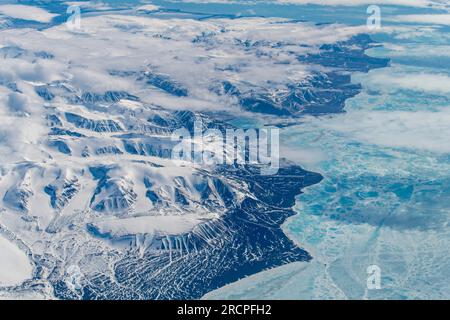 Vista aerea da 38.000 piedi delle montagne e delle colline sulla costa della Groenlandia nel circolo polare artico per lo più ricoperte di neve e basse nuvole hangi Foto Stock