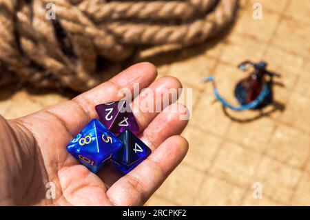 Mano che tiene tre dadi d8, due blu, uno viola, con mappa di battaglia RPG e statuetta sullo sfondo. Utilizzato per DND e altri giochi di ruolo Foto Stock