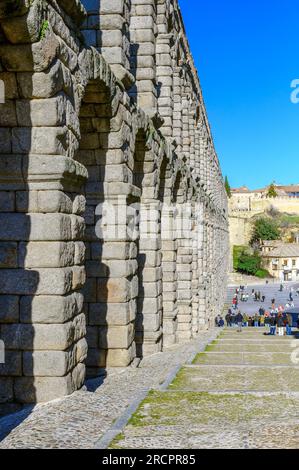 Segovia, Spagna - 11 febbraio 2023: Acquedotto romano. Strada acciottolata e piazza accanto alla struttura dell'acquedotto romano. I turisti o le persone sono nella dista Foto Stock