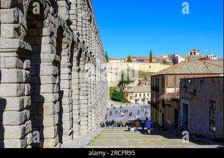 Segovia, Spagna - 11 febbraio 2023: Acquedotto romano. Strada acciottolata e piazza accanto alla struttura dell'acquedotto romano. I turisti o le persone sono nella dista Foto Stock