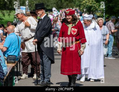 Neubrandenburg, Germania. 16 luglio 2023. In occasione dell'anniversario della città di 775 anni di Neubrandenburg, personaggi storici della città come il fondatore della città Herbord von Raven camminano davanti a un tavolo. Su una lunghezza di 775 metri, dal padiglione del ghiaccio al municipio, il più lungo tavolo festivo di Neubrandenburg è allestito lo stesso giorno. Dalle 14:00 alle 18:00, tutte le persone sono invitate a sedersi ai tavoli con il loro cestino da picnic, a conversare tra loro o a passeggiare lungo il percorso. Crediti: Stefan Sauer/dpa/Alamy Live News Foto Stock