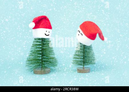 Due piccoli alberi di Natale in rosso Babbo Natale. Decorazione di abete artificiale. Bella imitazione di un piccolo albero di Natale, con Santa Cap su blu b Foto Stock