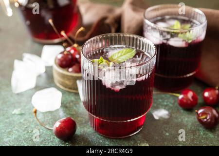 Fredda e rinfrescante Cherry cola in un bicchiere con ghiaccio su fondo di pietra, succo estivo. Foto Stock