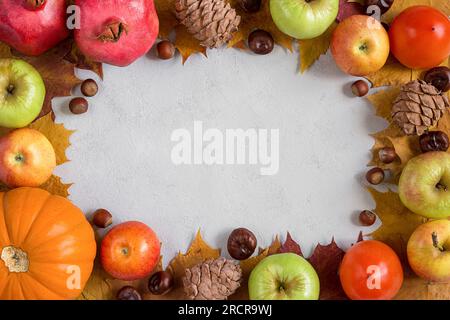 Cornice autunnale con foglie di acero giallo, noci, mele e zucca. Raccolta autunnale su sfondo grigio calcestruzzo con spazio di copia. Foto Stock