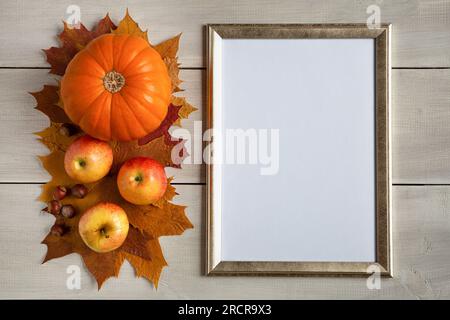 Natura morta autunnale con zucca d'arancia, mele e foglie d'acero piatte poggia su uno sfondo di legno bianco con cornice per il mockup posto per il testo Foto Stock