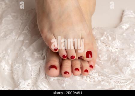 Primo piano dei piedi femminili con una bella pedicure rossa su pizzo bianco Foto Stock