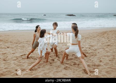Brezze marine e pose guerriere. Gruppo di persone che fanno yoga sulla spiaggia, in piedi in cerchio, esercitano esercizi asana Foto Stock