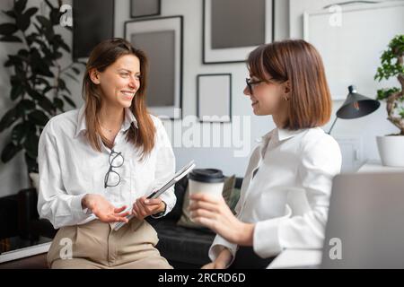 Allegri colleghi che si godono una pausa caffè, due donne d'affari che parlano, si incontrano e chiacchierano in ufficio Foto Stock