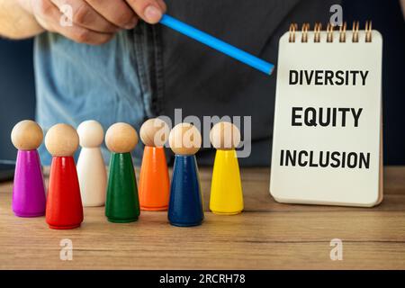 Figure di persone in miniatura di colori diversi, il concetto di diversità negli affari come valore positivo, Manager indica una lavagna con scritto Foto Stock