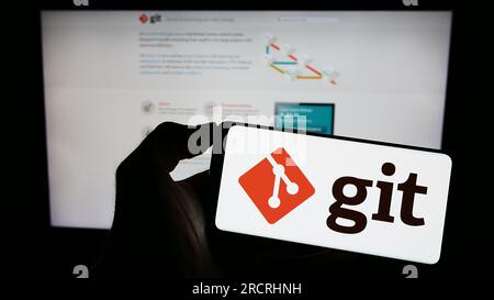 Persona che possiede il cellulare con il logo del sistema di controllo della versione distribuita Git sullo schermo davanti alla pagina Web. Concentrarsi sul display del telefono. Foto Stock