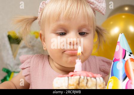 Una bambina di due anni fa spara una candela su una torta di compleanno, fa un desiderio Foto Stock