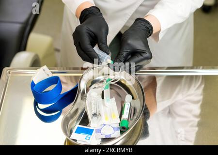 Prepararsi per l'esame del sangue. Il tecnico di laboratorio prepara l'ago a farfalla con adattatore luer per prelevare il sangue del paziente per l'analisi chimica del sangue. Raccogliere bl Foto Stock