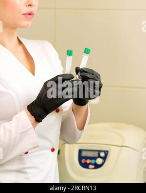 Mano infermiera in guanto medico tenendo provette di prova per prendere analisi del sangue. Provette per vuoto con gel eparinico per il prelievo ematico Foto Stock