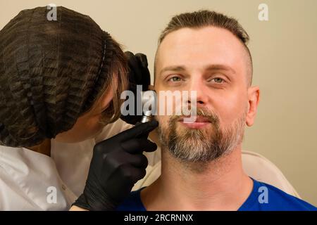 Medico dermatologo esamina nei e segni di nascita di pazienti maschi con dermatoscopio. Mantenimento preventivo del melanoma Foto Stock