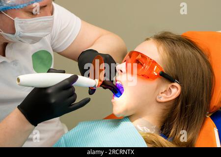 Studentessa su appuntamento dentistico. Dentista che lavora con la lampada UV per polimerizzazione dentale nella cavità orale. Restauro dei denti e riempimento con indurimento. Regula Foto Stock