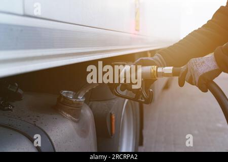 Un uomo tiene in mano una pistola, che ha inserito nel collo del serbatoio carburante, rifornisce il camion. Primo piano al sole. Foto Stock