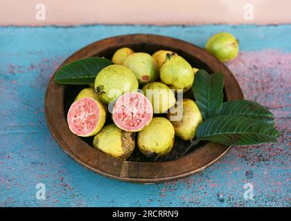 Guava maturi su un piatto di legno in giardino. Frutta tropicale biologica, cibo sano o concetto di dieta (Psidium guajava). Messa a fuoco selettiva. Foto Stock