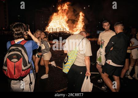 11 luglio 2023, Belfast, Irlanda: I giovani si radunano e posano di fronte alla pira in fiamme a Sandy Row. Il falò, alto parecchi piani, fu acceso a mezzanotte e nel giro di quattro minuti era crollato al suolo, Pyres, costruito con pallet di legno e talvolta pneumatici e altri materiali, sono costruiti in tutta l'Irlanda del Nord nei quartieri protestanti per l'anno 11 luglio, O celebrazioni dell'undicesima notte per commemorare la conquista guelamita degli anni '1690, che ha dato inizio all'ascendenza protestante in Irlanda. Le pire sono generalmente adornate con il tricolore irlandese e altri reg Foto Stock