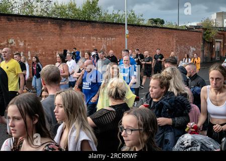 11 luglio 2023, Belfast, Irlanda: La gente del posto si riversa per le strade dopo che una band di tamburi e flauto ha iniziato una marcia che procederà attraverso i labirintici vicoli e le tenute di Sandy Row. Canzoni come "King Billy's on the Wall" sono cantate così come canti di insulti contro il Papa e il nazionalismo cattolico. Le pire, costruite con pallet di legno e talvolta pneumatici e altri materiali, sono costruite in tutta l'Irlanda del Nord nei quartieri protestanti per l'annuale 11 luglio, o celebrazioni dell'undicesima notte per commemorare la conquista guelamita degli anni '1690, che ha dato inizio all'ascesa protestante Foto Stock