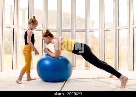 Mamma e figlia giovani si divertono con la palla fitness in palestra Foto Stock