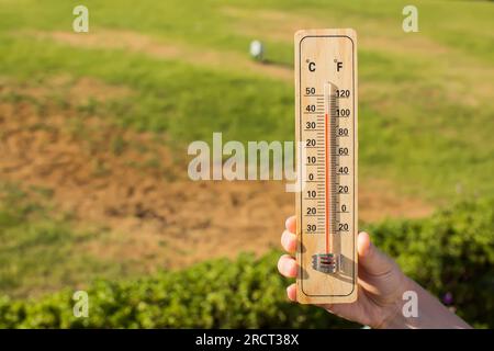 Clima caldo. Termometro in mano davanti all'erba secca durante l'onda di calore. Concetto di alta temperatura e meteorologia Foto Stock