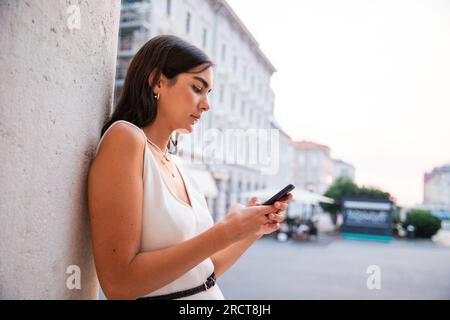 Una ragazza scrive messaggi con il suo smartphone mentre si trova in centro città Foto Stock