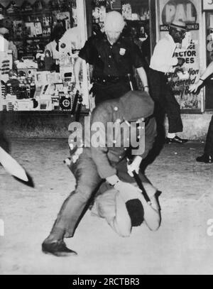 New York, New York: 1964 Un poliziotto club' un sospetto lanciabottiglie giacente sulla strada di Harlem. Foto Stock