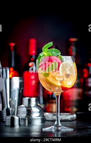 Rosу sangria bevanda alcolica estiva con vino rosa, pesca, arancia, lime e ghiaccio. Fondo nero del banco, strumenti e bottiglie in acciaio Foto Stock