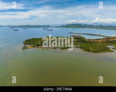 Isola tropicale e baia marina con cargo e nave mercantile. Cieli azzurri e nuvole. Mindanao, Filippine. Seascape. Foto Stock