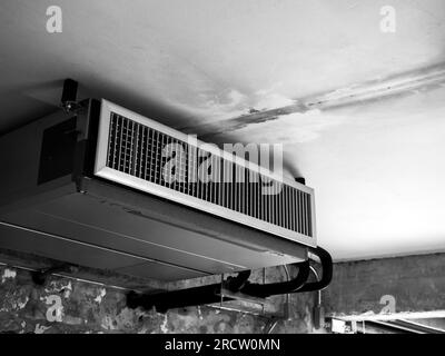 Macchina nera, aria condizionata moderna, sistema di ventilazione a soffitto decorato sul soffitto in una vecchia fabbrica di costruzioni bianche, stile loft Foto Stock