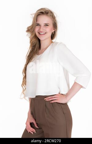 Giovane donna bionda felice con un sorriso toothy e capelli lunghi che guarda la fotocamera, posare su sfondo bianco. Ritratto di emozioni positive femminili europee Foto Stock