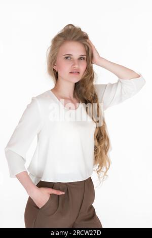 Giovane donna ben vestita e genuina di 21 anni che posa e guarda la fotocamera su sfondo bianco. Donna bionda europea con capelli lunghi Foto Stock