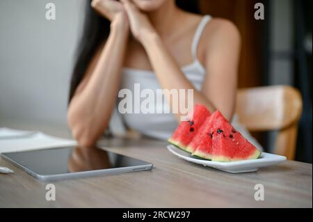 Immagine ravvicinata di un piatto con cocomeri su un tavolo con una donna surriscaldata sullo sfondo. estate calda, attacco di calore Foto Stock